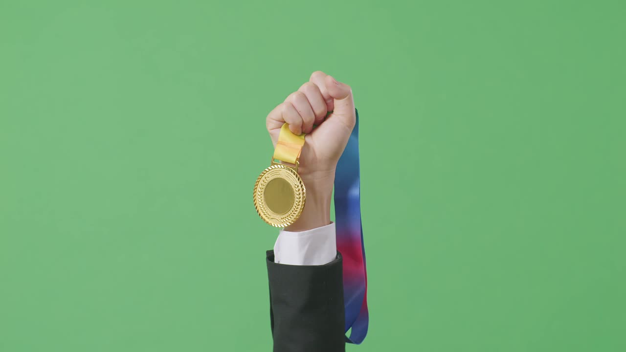 cerca de la mano del hombre de negocios sosteniendo una medalla de oro en el aire para celebrar la victoria como el primer ganador en el fondo de la pantalla verde en el estudio