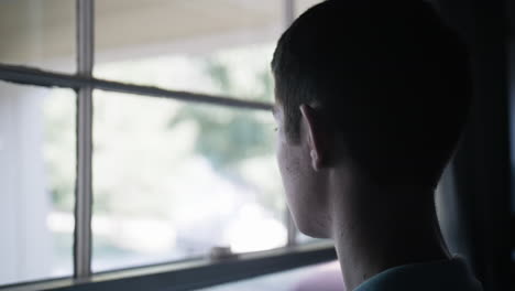 a young man, teenager looking outside window in cinematic slow motion