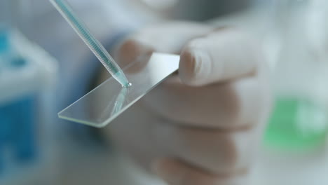 Woman-laboratory-technician-applying-drops-of-blood-on-glass-slide-from-pipette-in-lab-in-slow-motion-hands-in-latex.-High-quality-4k-footage