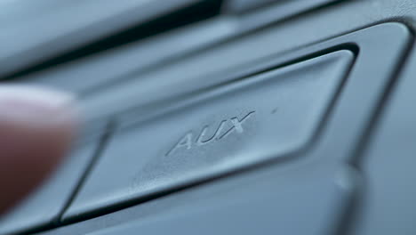 close up of a finger pushing the aux button on a car dash