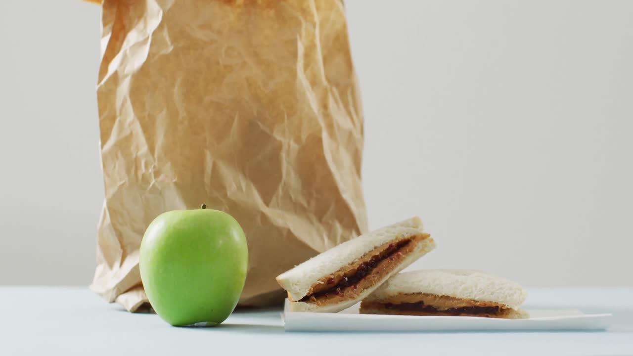 sándwich de mantequilla de maní y jalea con manzana y bolsa de papel contra un fondo blanco