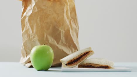 sándwich de mantequilla de maní y jalea con manzana y bolsa de papel contra un fondo blanco