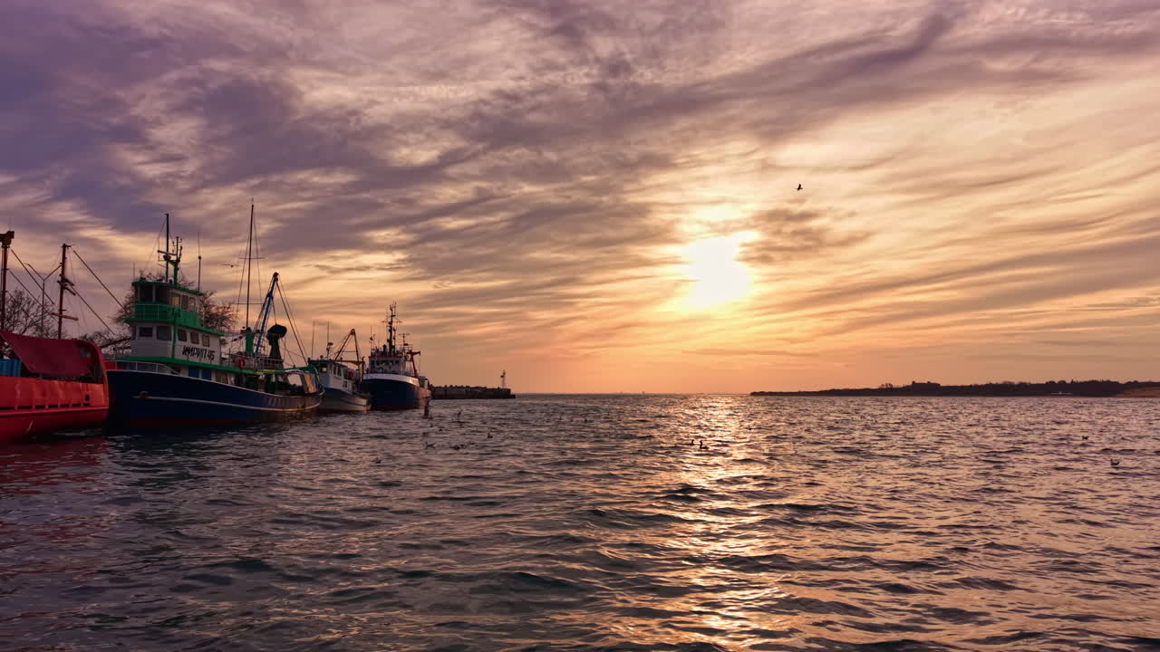 Barche da pesca riposano in tranquillità al tramonto lungo il porto sereno, dipingendo il cielo con vivaci tonalità arancioni e viola mentre il giorno lascia spazio alla notte.