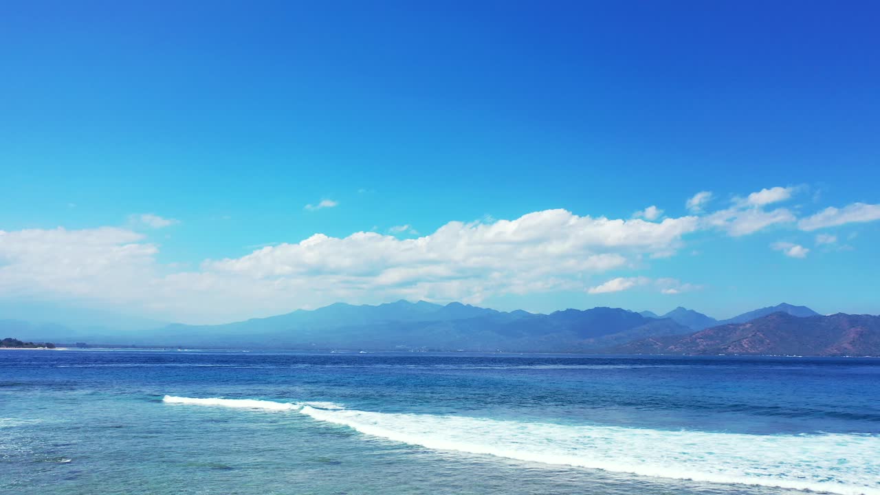 밝은 푸른 하늘과 하얀 구름이 하얀 파도가 거품을 내며 푸른 바다와 경계를 이루는 산 지평선 뒤에 떠오르는 생생한 일출의 색상