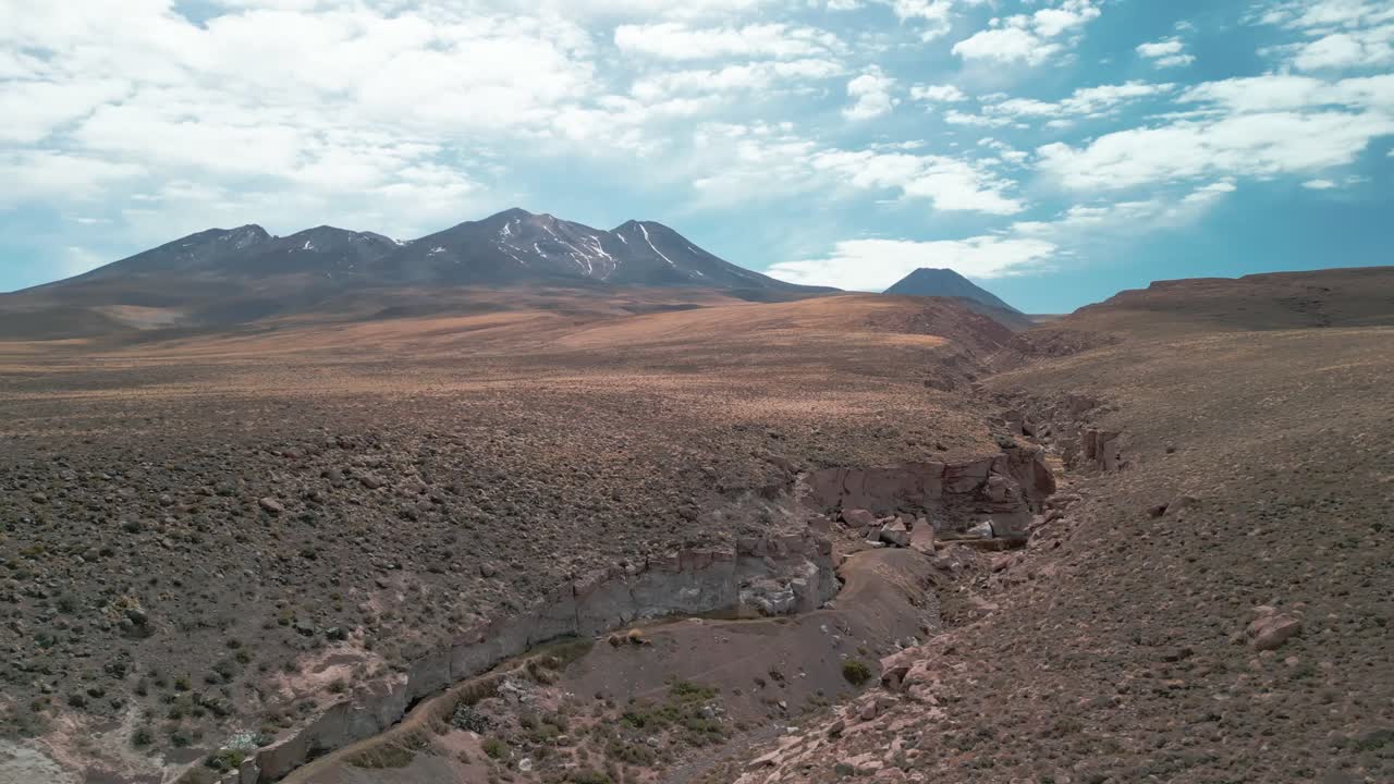 drone volando sobre el borde de un gran cañón en el desierto chileno con un volcán en el fondo