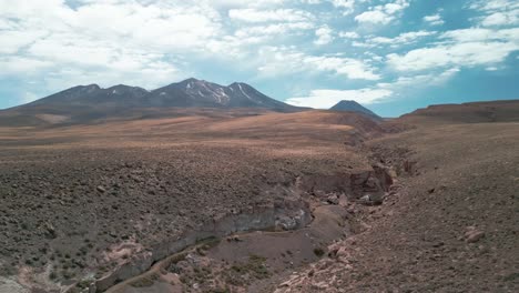 Drone-flying-over-the-edge-of-a-big-canyon-in-the-Chilean-desert-with-a-volcano-on-the-background