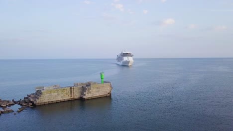 Aerial-view-of-large-white-cruise-liner-Seven-Seas-Splendor-arriving-at-the-port-of-Liepaja-,-early-morning-golden-hour,-water-transportation,-Baltic-sea,-vacation,-wide-shot-moving-forward