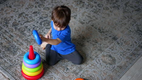 small baby boy sitting on the floor playing. lovely child assembles the toy pyramid. top view.