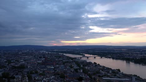 Sky-over-Mainz-with-a-drone-aerial-at-magic-hour-night-circling-with-the-cathedral-and-the-dark-Rhine-river-water-in-the-background-showing-a-colorful-sky