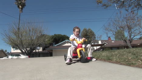 a girl loses her footing on a plastic tricycle and rolls down a driveway