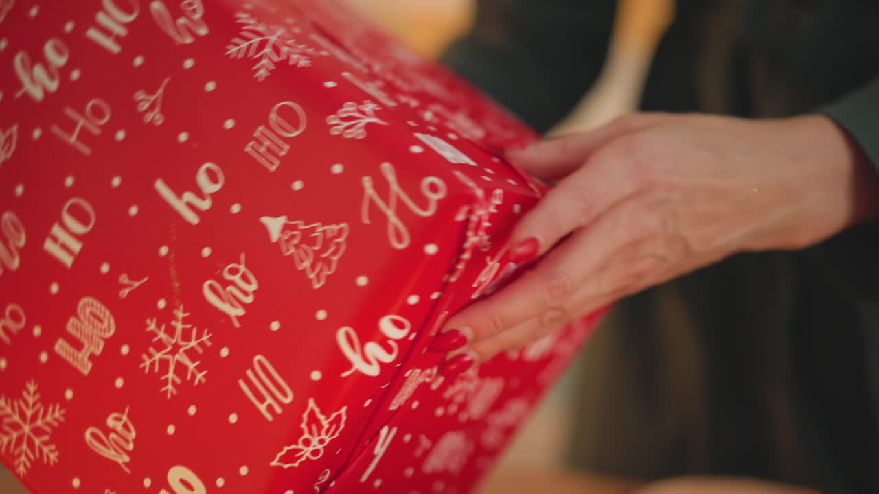 Close-up de mãos embrulhando presente de Natal, papel vermelho estampado com motivos