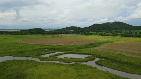 aerial reverse footage revealing hills, lake, farmlands, and a marshy land below then the railroad, muak klek, saraburi, thailand