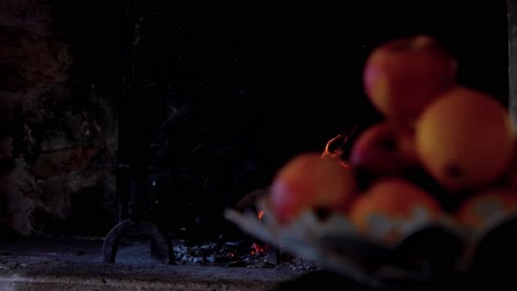 In-the-foreground-a-salad-bowl-of-apples,-in-the-background-a-fire-in-a-fireplace-with-logs