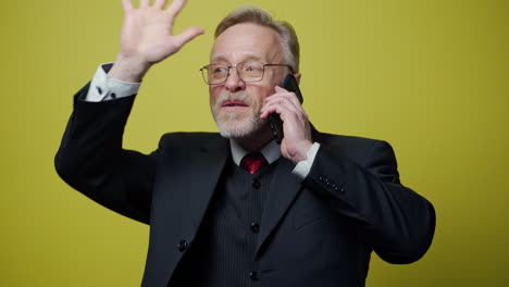 happy senior businessman talking the phone. portrait of a mature man in black costume speaking on the mobile phone and gesticulating a lot isolated on yellow.