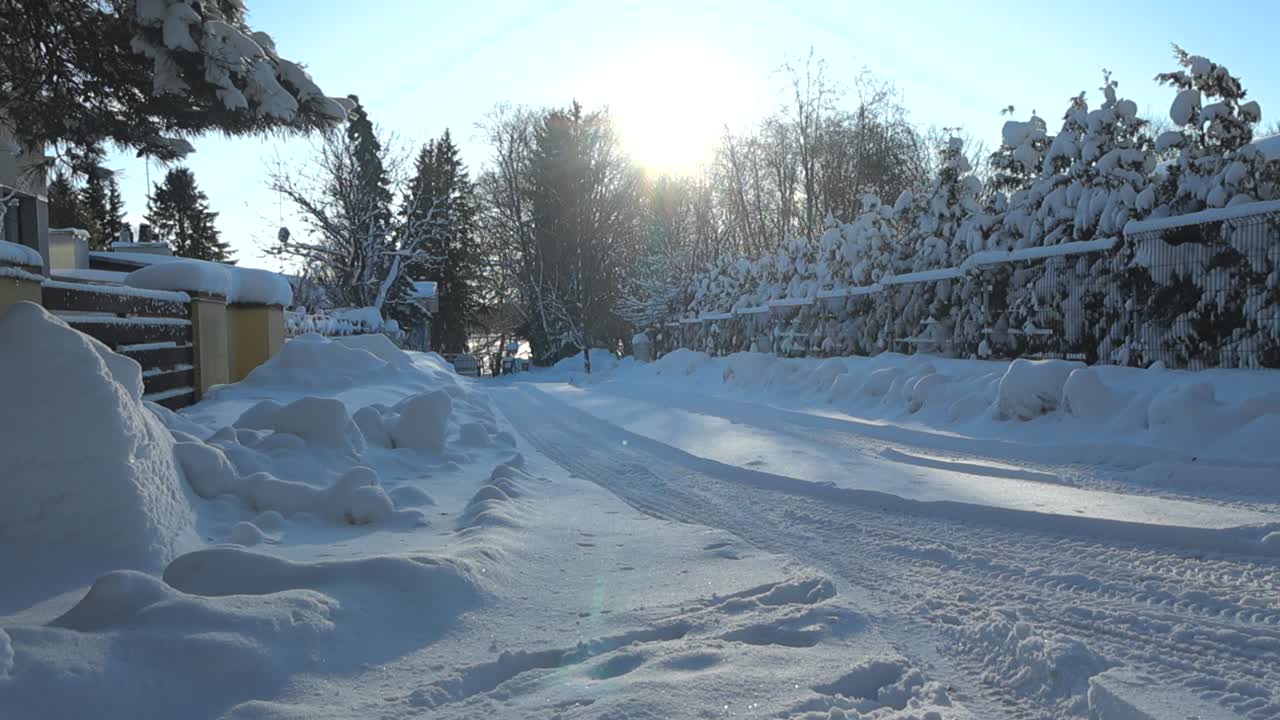 Gorgeous footage of an urban street with large piles of white fluffy snow in between the streets during a sunny cold winter day while pine trees and bushes are covered with dense and thick white snow.