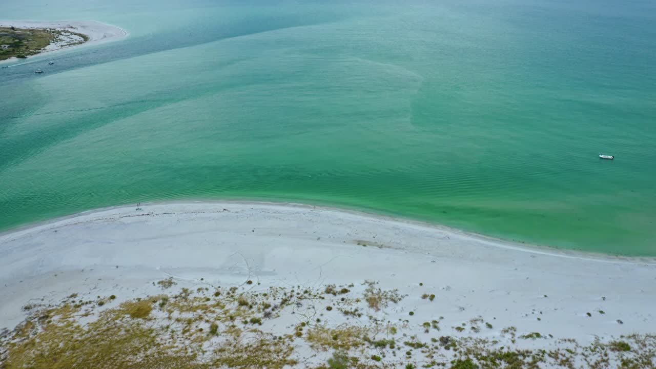 A secluded shoreline curves around pale sand while modern waterfront homes stand beside calm turquoise water, conveying a tranquil sense of open coastal living