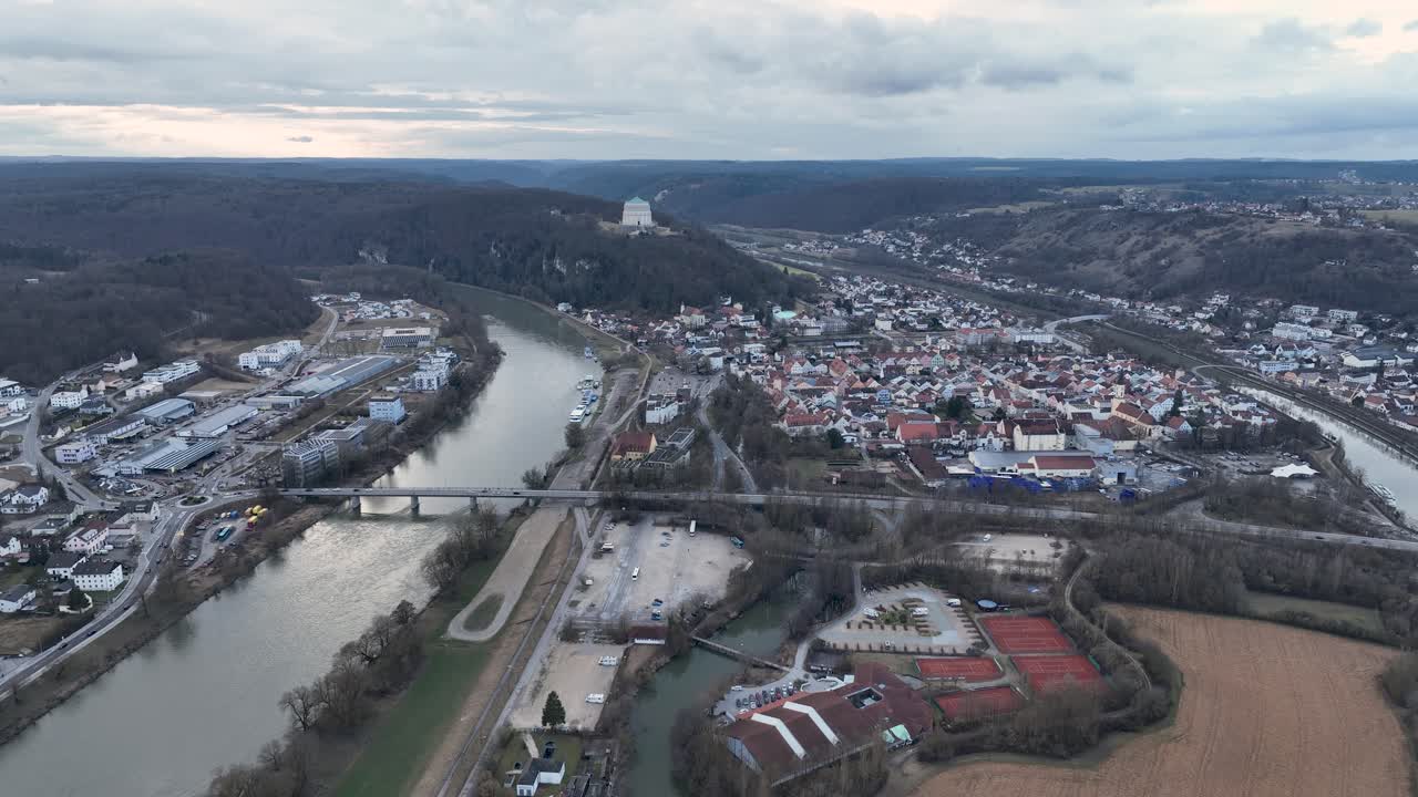 A tranquil drone shot of the Kelheim waterfront on the Danube River, with boats docked and the famous Befreiungshalle monument visible in the distance