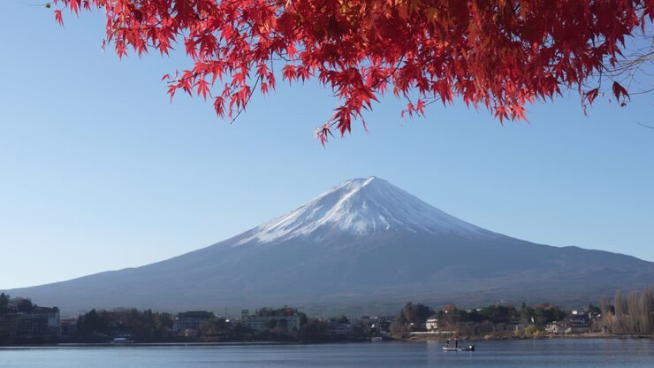 Il Monte Fuji in una tranquilla giornata autunnale con foglie rosse nel vento e un calmo lago Kawaguchiko, Giappone.