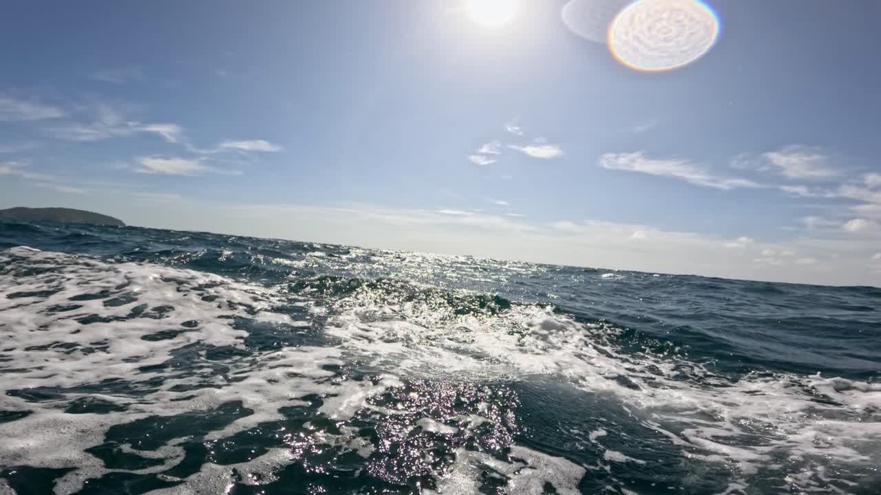 Dynamic ocean waves captured from a moving boat in Phuket, Thailand, under bright sunlight and clear skies