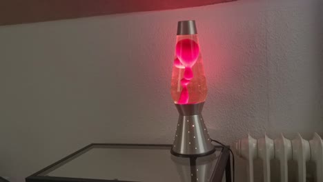 lámpara de lava resplandeciente y burbujeante sobre una mesa de cristal junto a un radiador montado en la pared