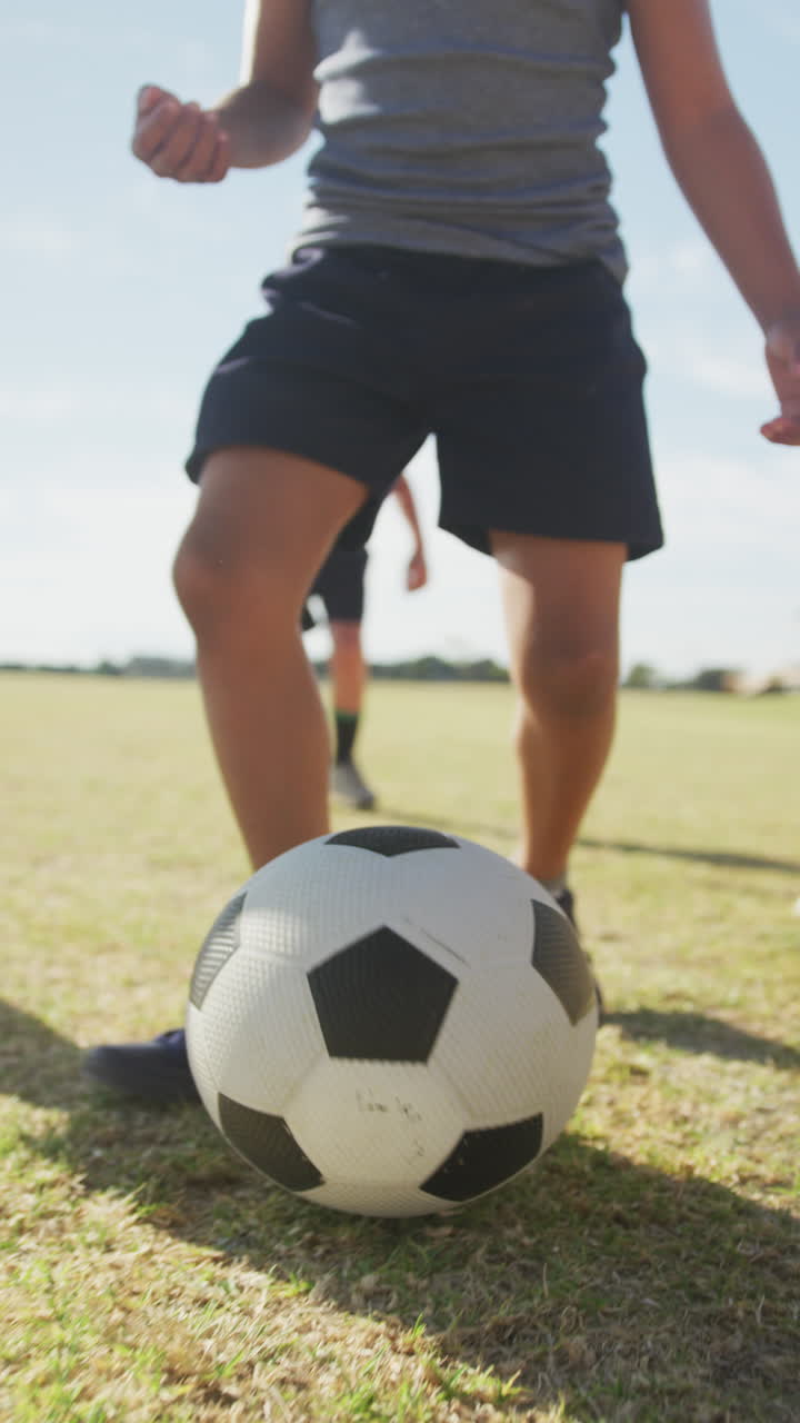Video vertical de escolares diversos felices jugando al fútbol juntos