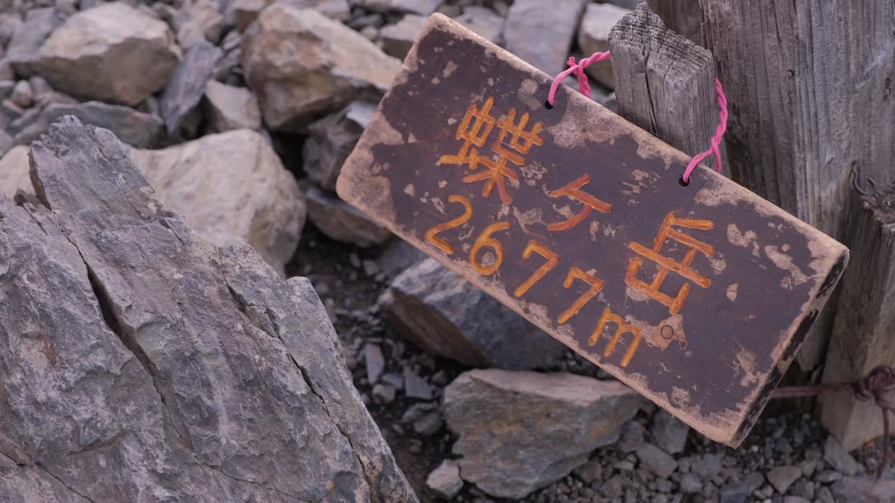 Close-up of a weathered wooden sign reading “Chogatake 2677m,” resting among rocks on the mountain summit