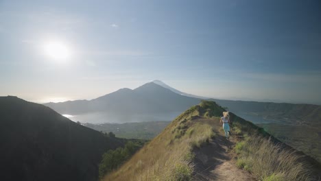 sportive blond woman running on mountain trail ridge towards lookout, sense of freedom, bali