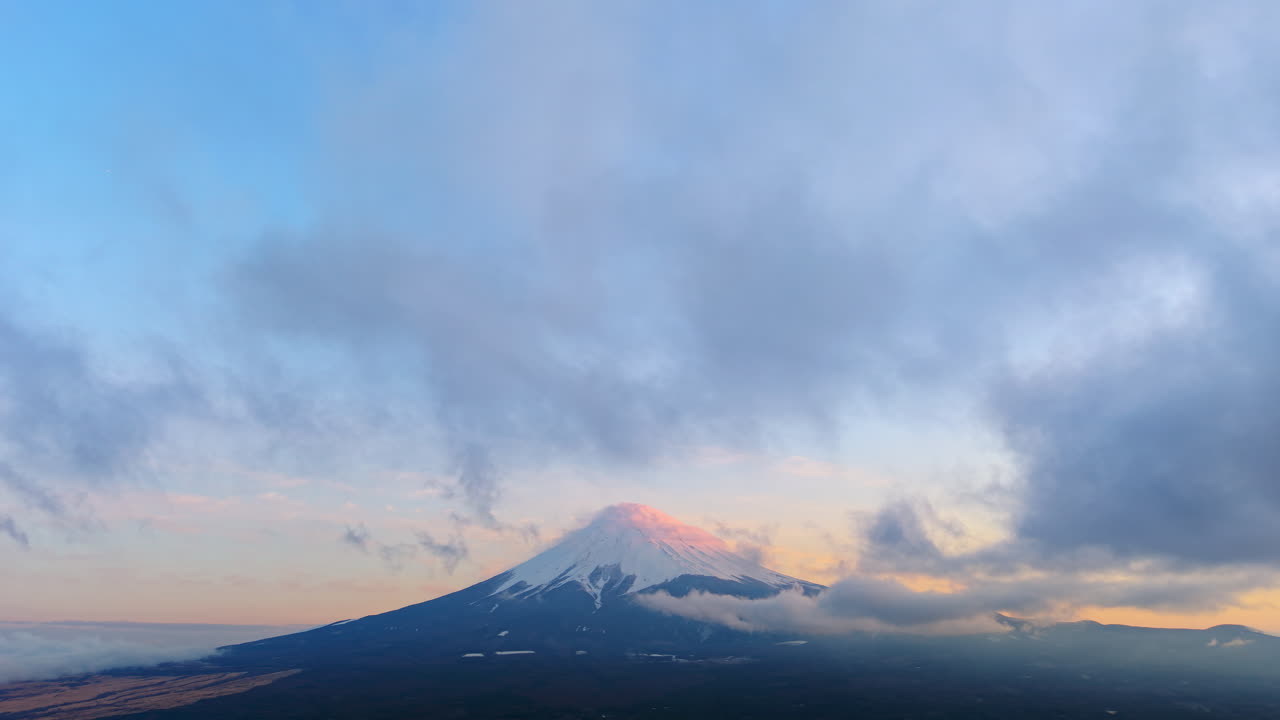 Aerial drone view of Mount Fuji with snow at the top and clouds moving around in daylight