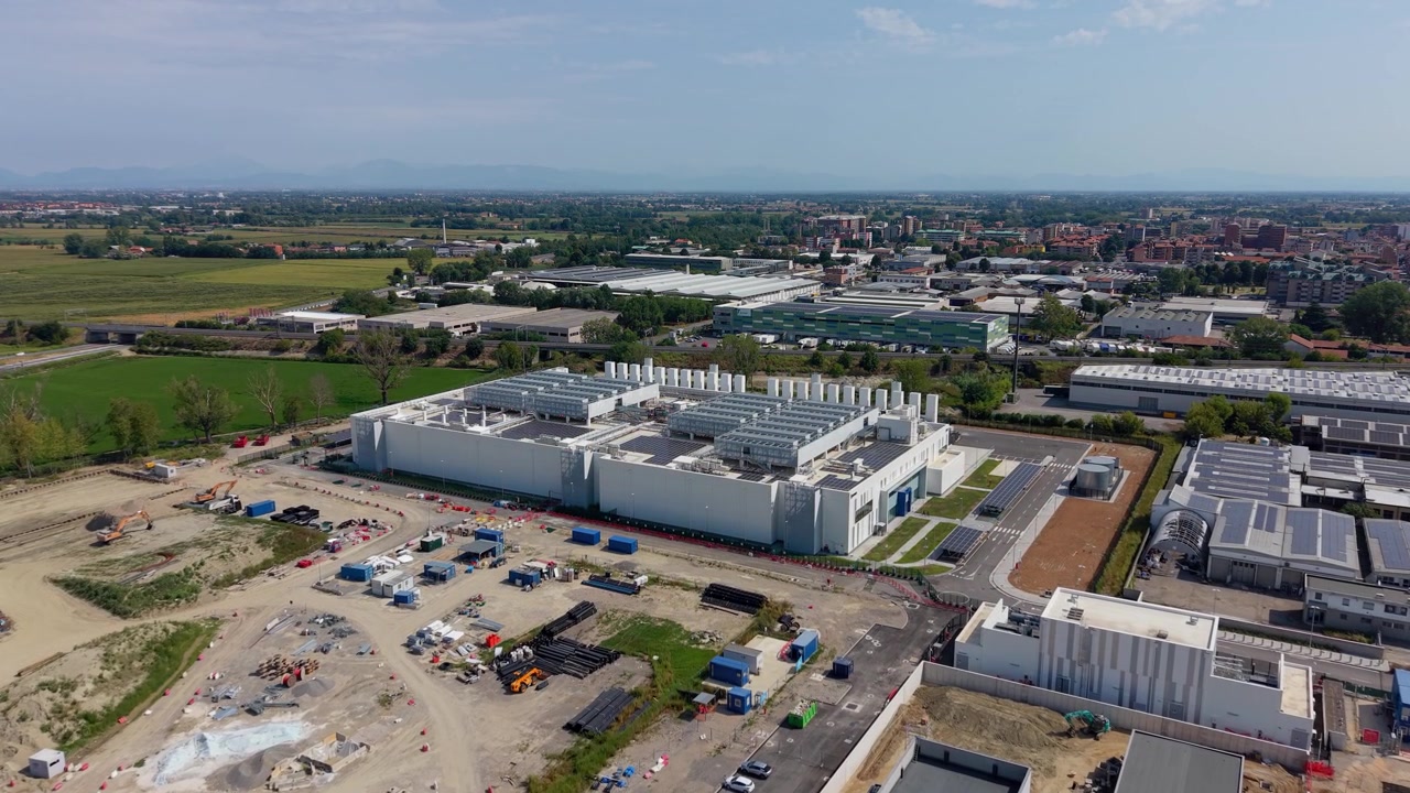 Vista aérea de un gran campus de centro de datos cerca de Milán, con una extensa infraestructura digital y paneles solares en el tejado que soportan operaciones modernas de computación en la nube.