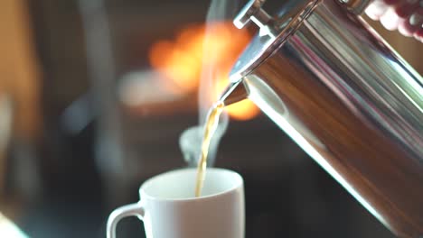 slow motion pouring steaming hot french press coffee into a mug in front of a glowing fireplace