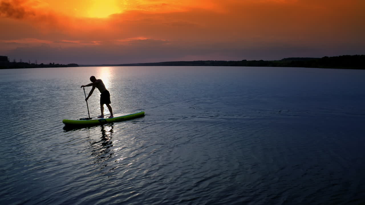 Young Man SUP Boarding. Aerial view of strong man swimming surfing boat