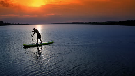 Young Man SUP Boarding. Aerial view of strong man swimming surfing boat
