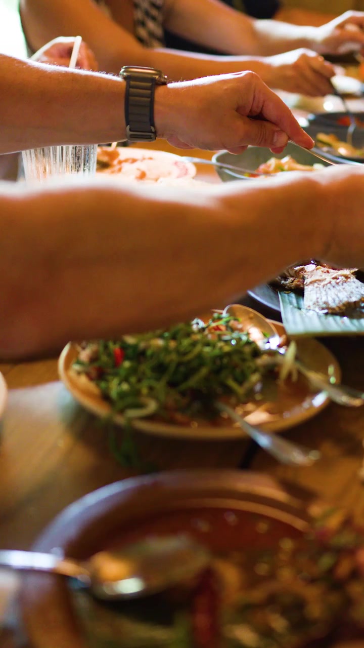 Group enjoys traditional Thai dishes, grilled fish, and spicy salad in warm, natural restaurant lighting