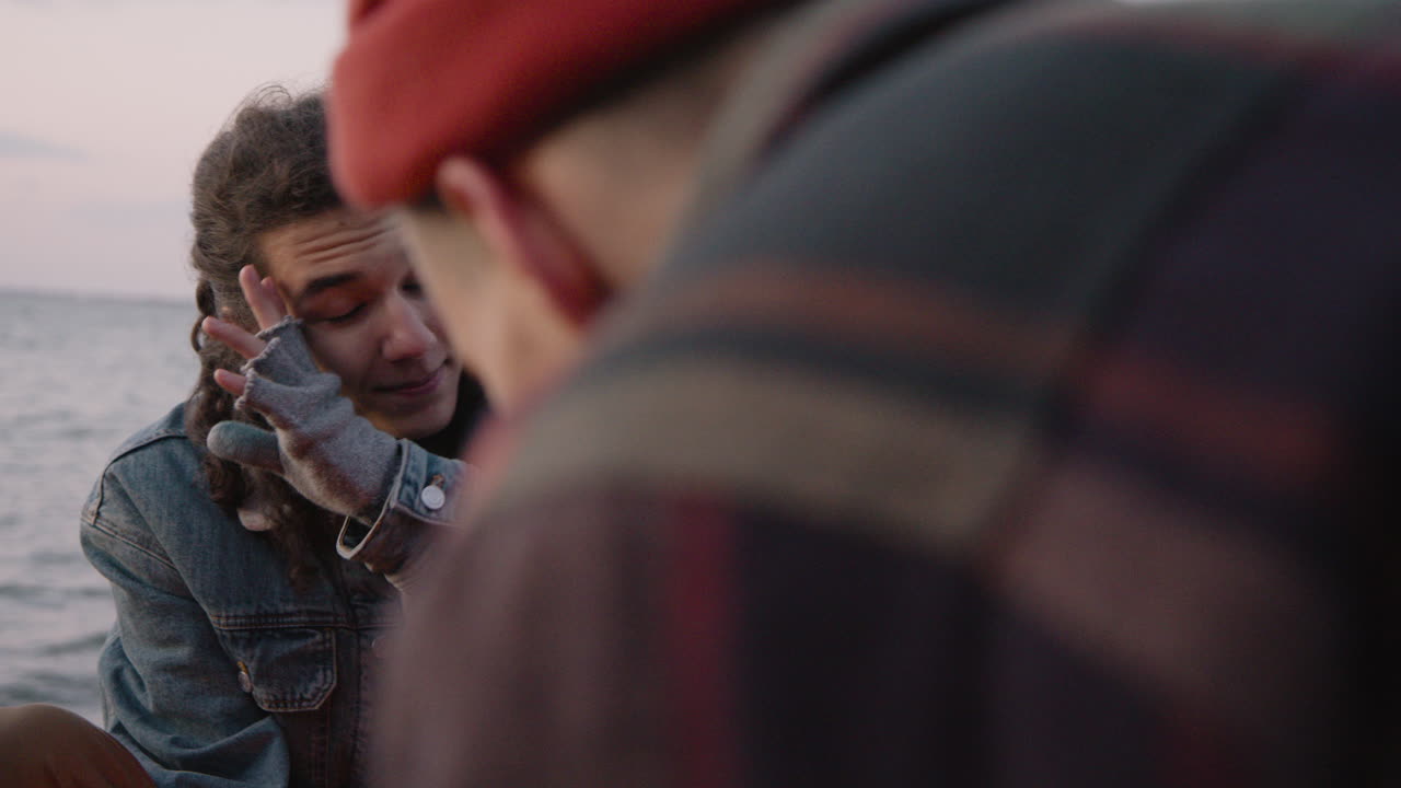 카메라는 모닥불 근처에 그녀 앞에 앉아 있는 친구와 이야기하는 십대 소년에 초점을 맞춥니다.