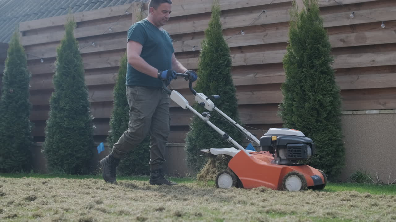 Man Scarifying Lawn in Backyard with Dethatcher Machine