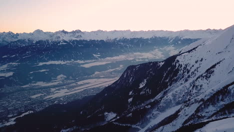 Innsbruck,-Austria---view-over-city-Innsbruck-in-the-valley-with-snowy-Alps-during-sunset-|-Aerial-View