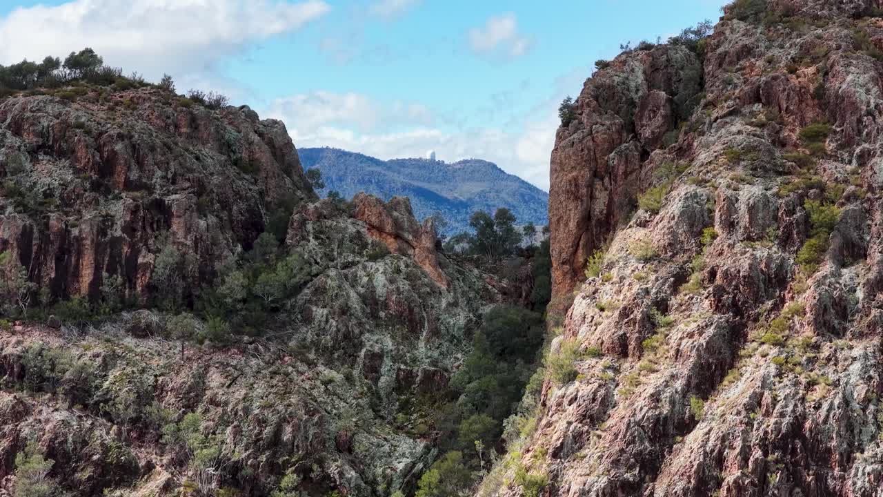 Drone camera smoothly pans across rugged Split Rock cliffs, revealing dramatic rock formations, sparse vegetation, and distant mountain ranges under bright daylight