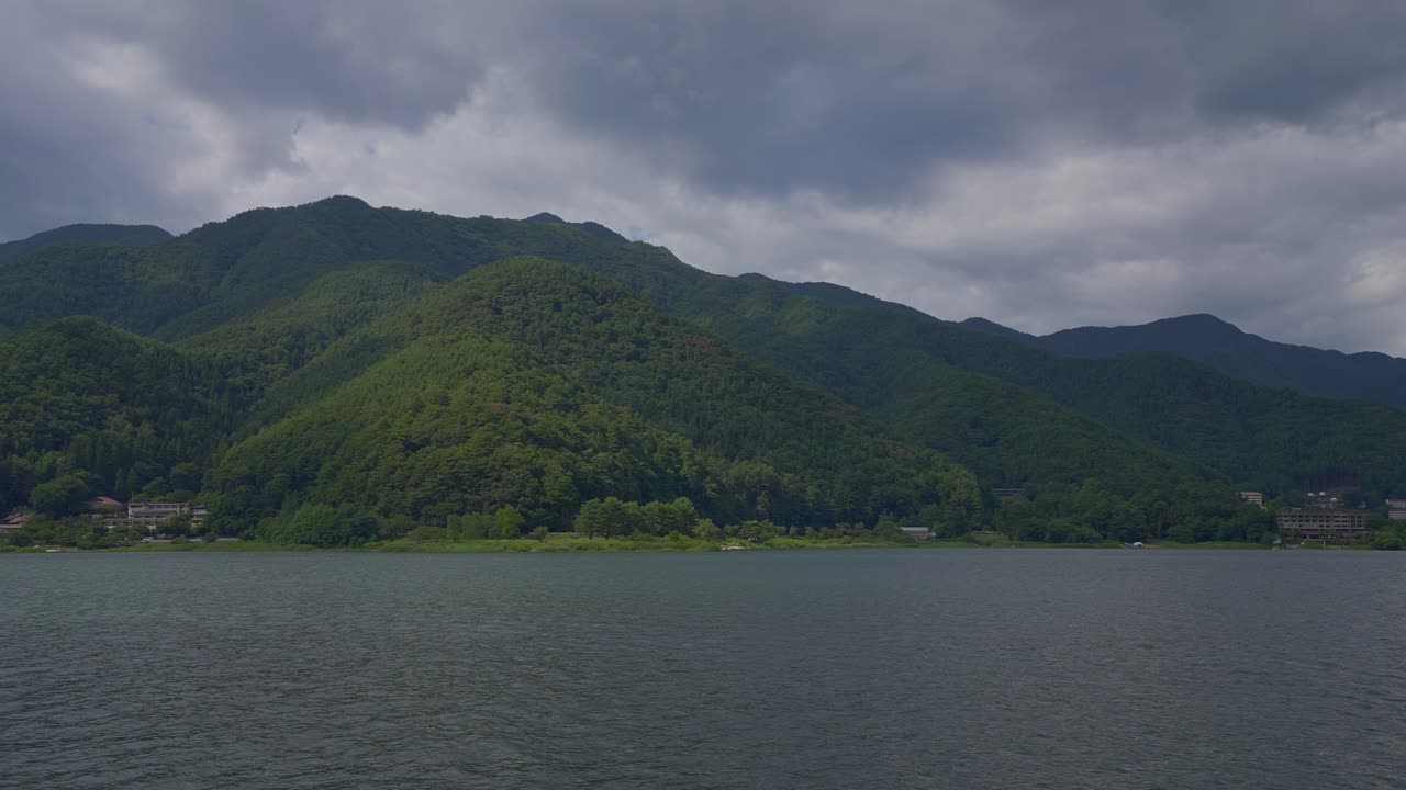 Traverse the serene lake, where the vista unfolds with green hills cascading into the Japanese waters from the boat's viewpoint during a cloudy day