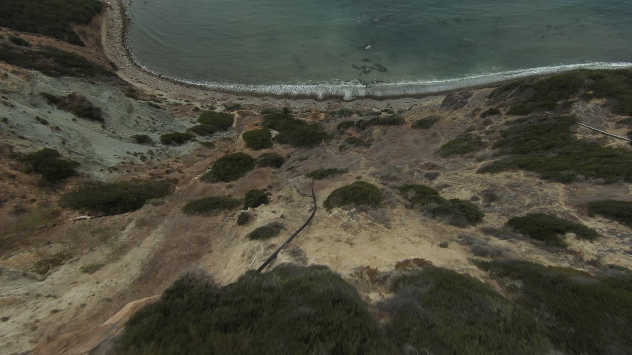 volando sobre un acantilado hacia el océano y la playa y luego a lo largo del terreno rocoso de la costa - vista aérea en primera persona