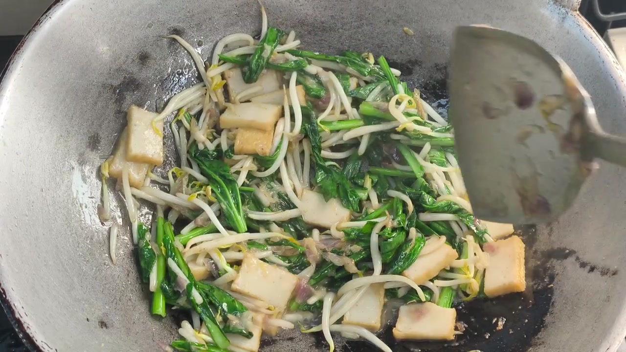 Le verdure di senape, i germogli di soia e le polpette di pesce sono fritti velocemente in un wok caldo. Vengono aggiunti ingredienti aromatici come cipolle e acciughe. Questo crea un pasto delizioso e saporito che mantiene le verdure croccanti.