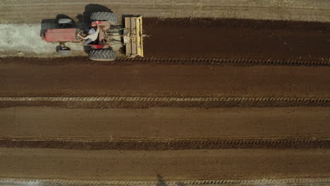 Rising-drone-shot-of-a-tractor-tilling-the-field,-establishing-view-of-a-farmer's-vehicle-preparing-the-land