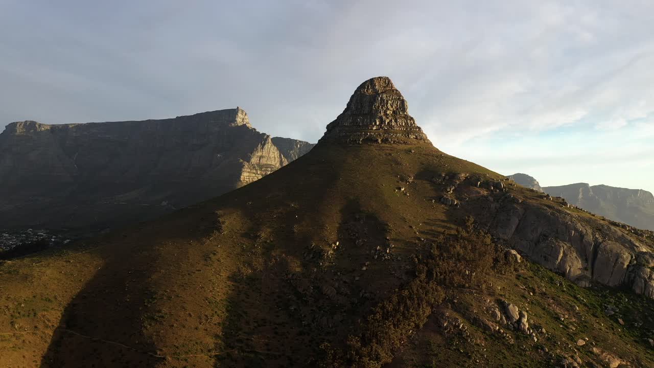 toma aérea cinematográfica del pico de la cabeza de león de ciudad del cabo con la montaña de la mesa durante la puesta de sol de la hora dorada volando de lado