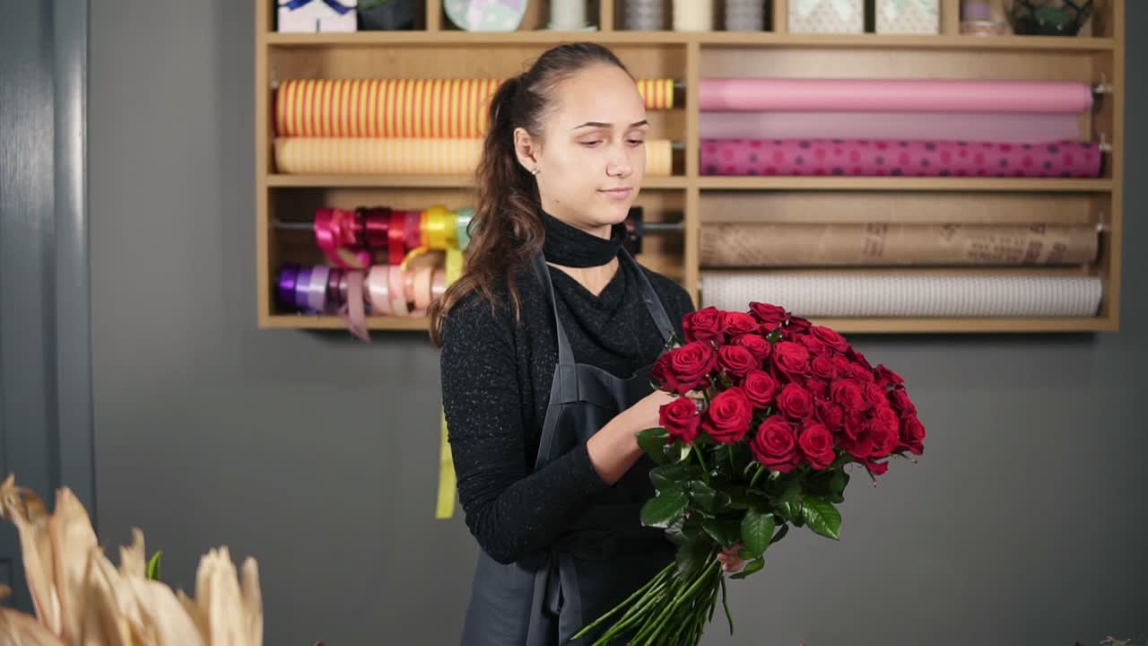 un ramo perfecto de rosas rojas de un florista profesional: una florista joven y atractiva arregla un ramo de hermosas rosas rojas