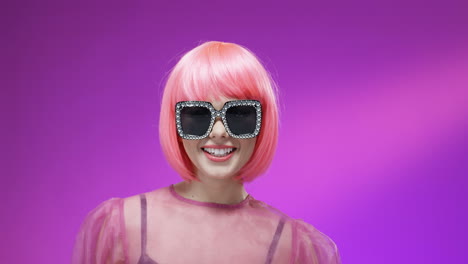 portrait of stylish woman wearing a pink wig and glamourous sunglasses, smiling to camera and blowing kisses