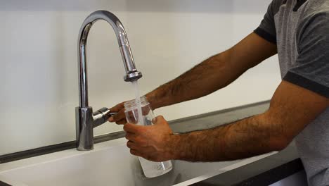 a still shot of a guy filling up a water bottle from the tap next to the counter