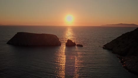 aerial trucking pan tilt up, long shadows of rocky islands silhouettes, yellow glowing sunset on varvarousa beach