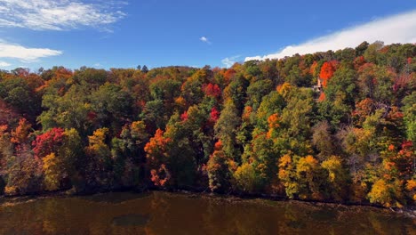 An-aerial-view-over-a-reflective-lake,-surrounded-by-colorful-trees-during-the-fall-foliage-in-upstate-NY