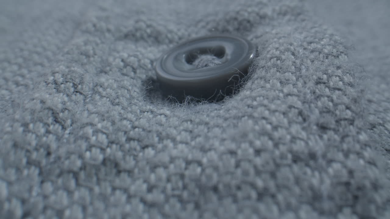 Macro Shot of a Gray Button Being Unbuttoned from Knitted Fabric
