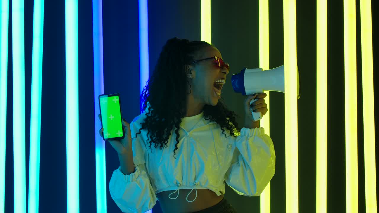 retrato de una joven y encantadora mujer afroamericana emocionalmente dice algo en el altavoz y muestra un teléfono inteligente con una tecla de croma de pantalla verde. promoción, publicidad. cámara lenta