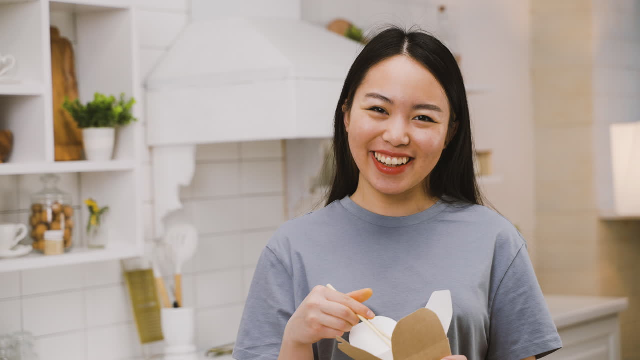 menina japonesa feliz comendo ramen para viagem enquanto olha para a câmera  e sorri 1